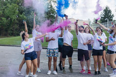 A group of students throw colored poweder into the air at a festival.